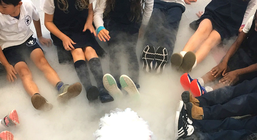 Kids sitting in a circle with legs straight out surrounding dry ice and smoke cause from the dry ice.