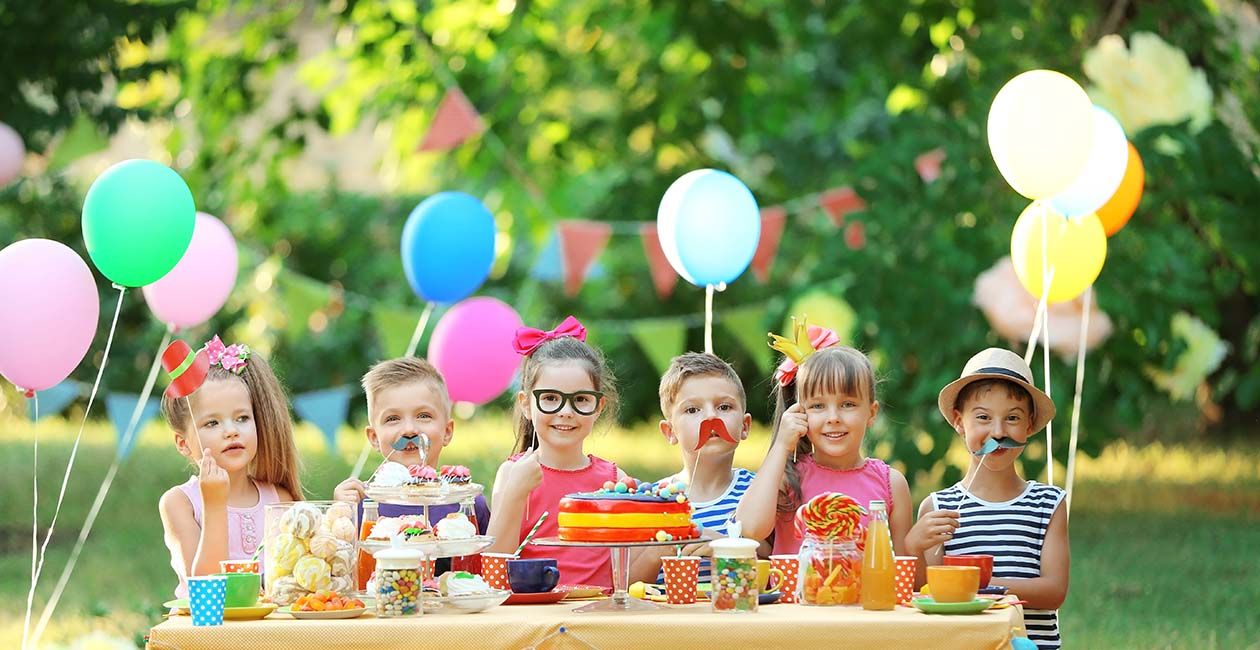 Kids celebrating birthday in park with glasses, mustache and hat props