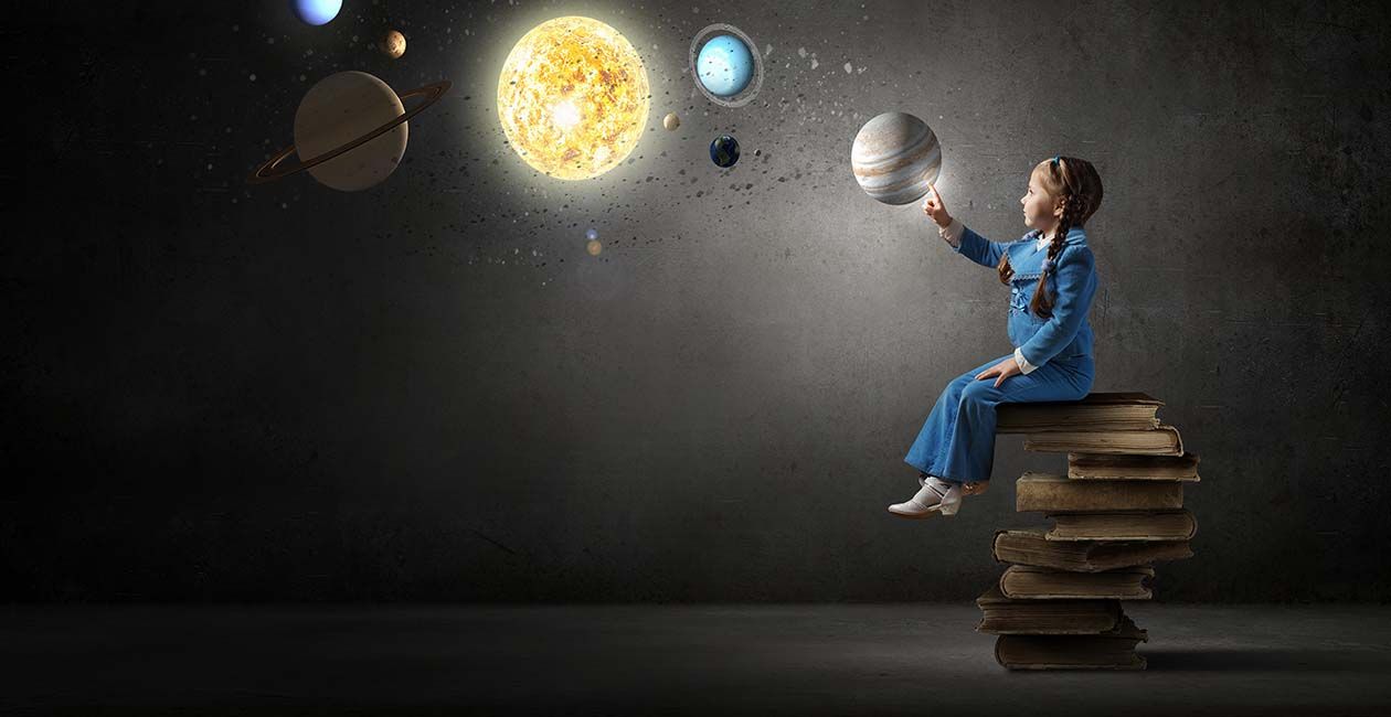 A girl sitting on a stack of books point to planets in the air