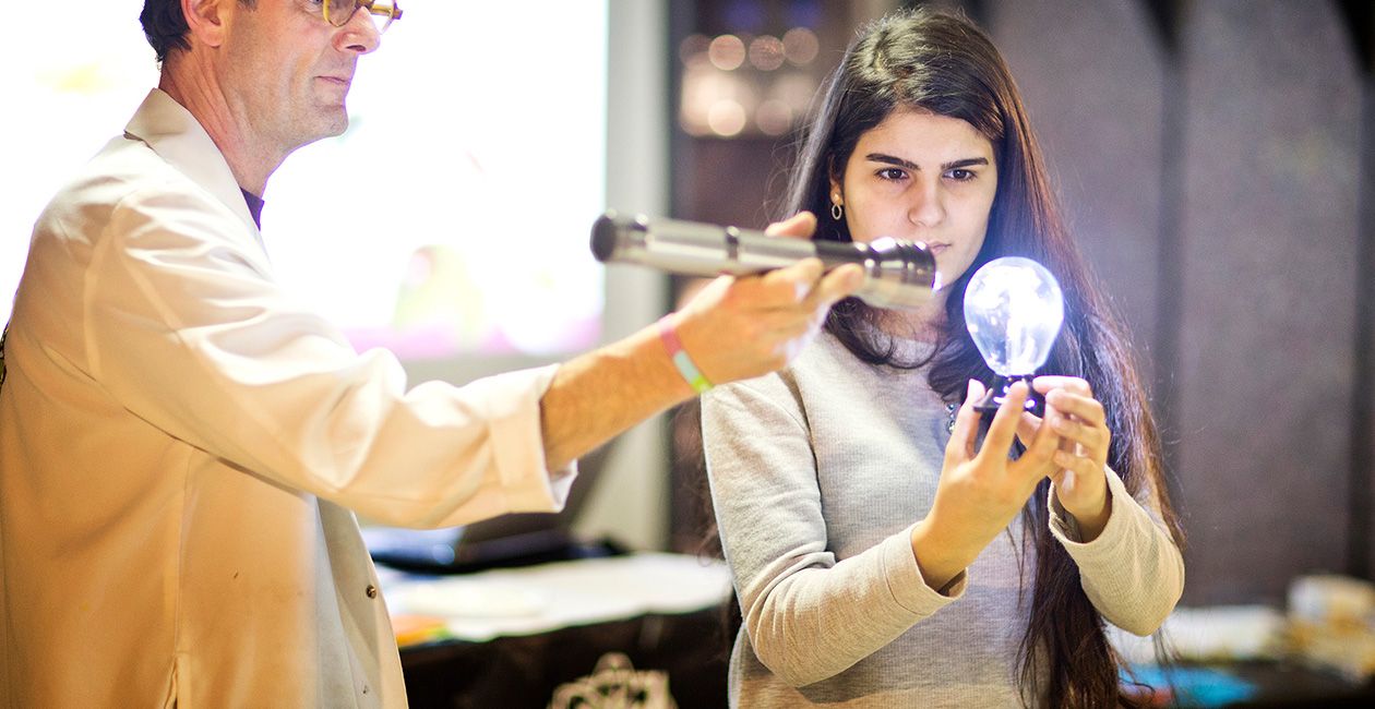 Mad scientist holding flash light point it at a light bulb that a girl is holding
